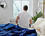 Man sitting up in bed, next to Navy Cooling Blanket