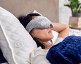Woman sleeping in bed on a Gravity Pillow. She is wearing a Weighted Sleep Mask and has a Navy Gravity Blanket pulled over her.