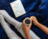 Woman holding a coffee cup over a Navy Gravity Blanket.