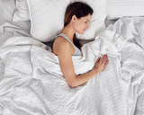 Woman sleeping under white blanket.