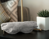 The Weighted Sleep Mask on a bedside table next to a plant.  